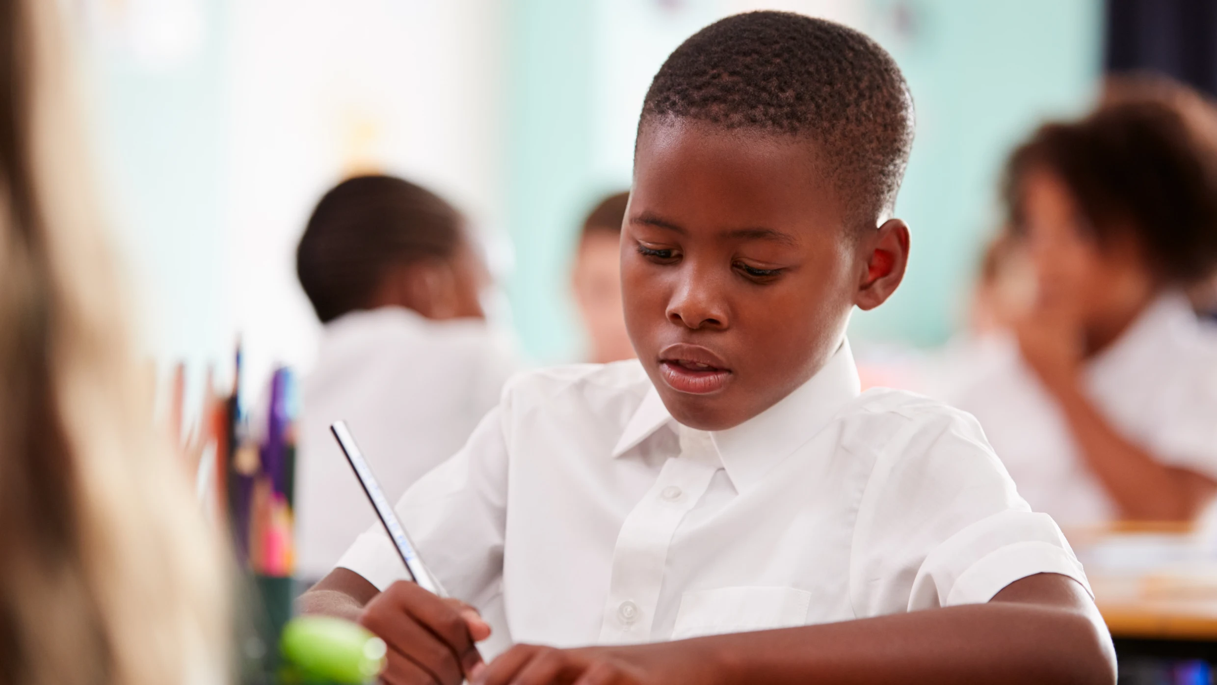 Primary school pupil concentrating while writing at a desk in the classroom.