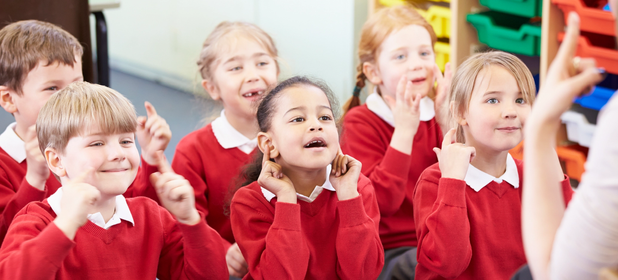 Primary school children in red uniforms learning sign language together.