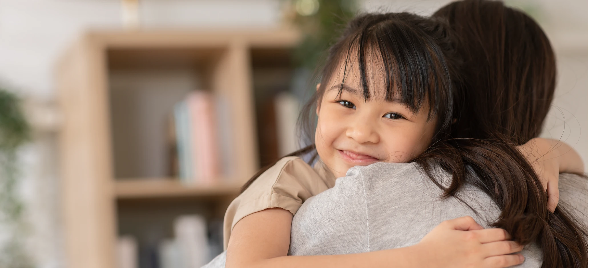 A young child smiling while hugging an adult indoors.
