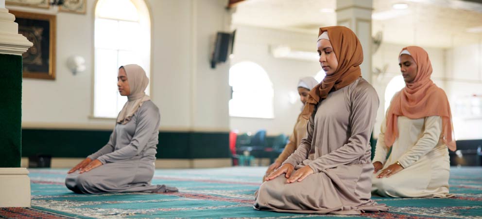 Women kneeling in prayer inside a mosque.