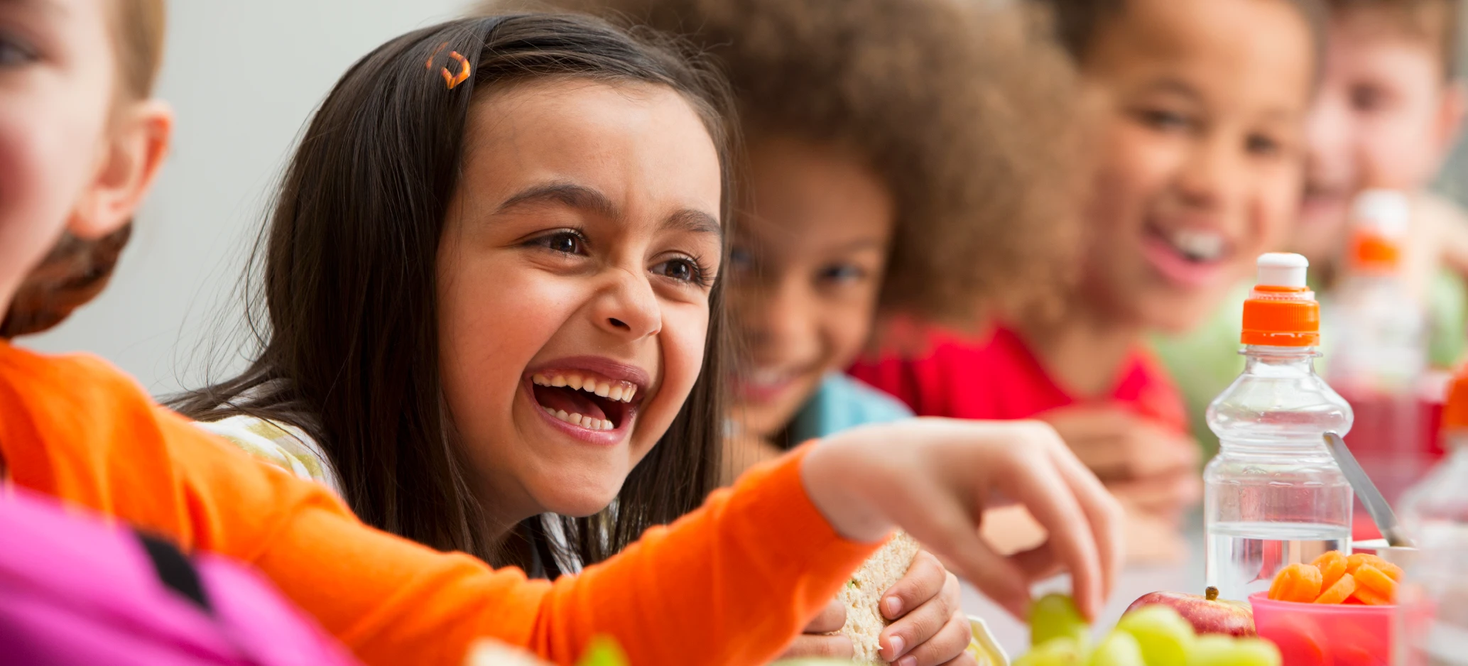 Primary school pupils laughing and sharing fruit and snacks during a healthy lunchtime at school