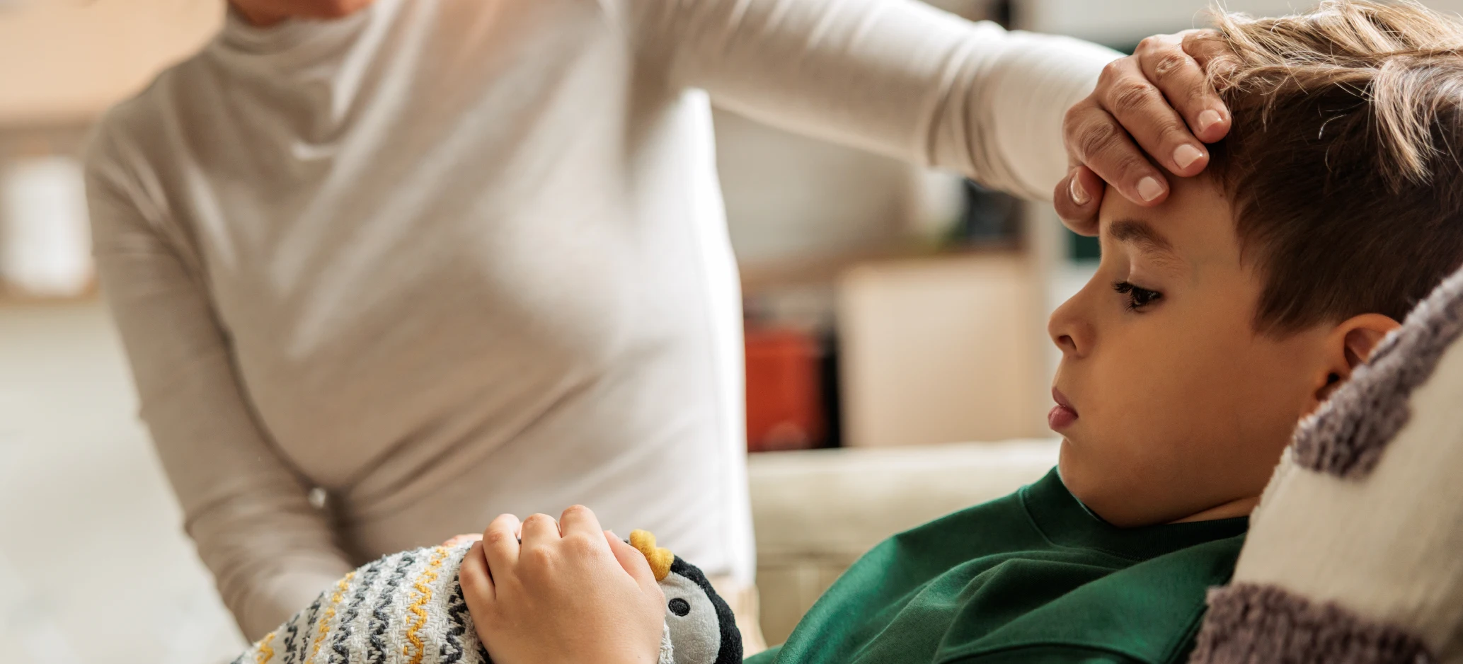 Adult checking a child’s temperature while the child rests on a sofa
