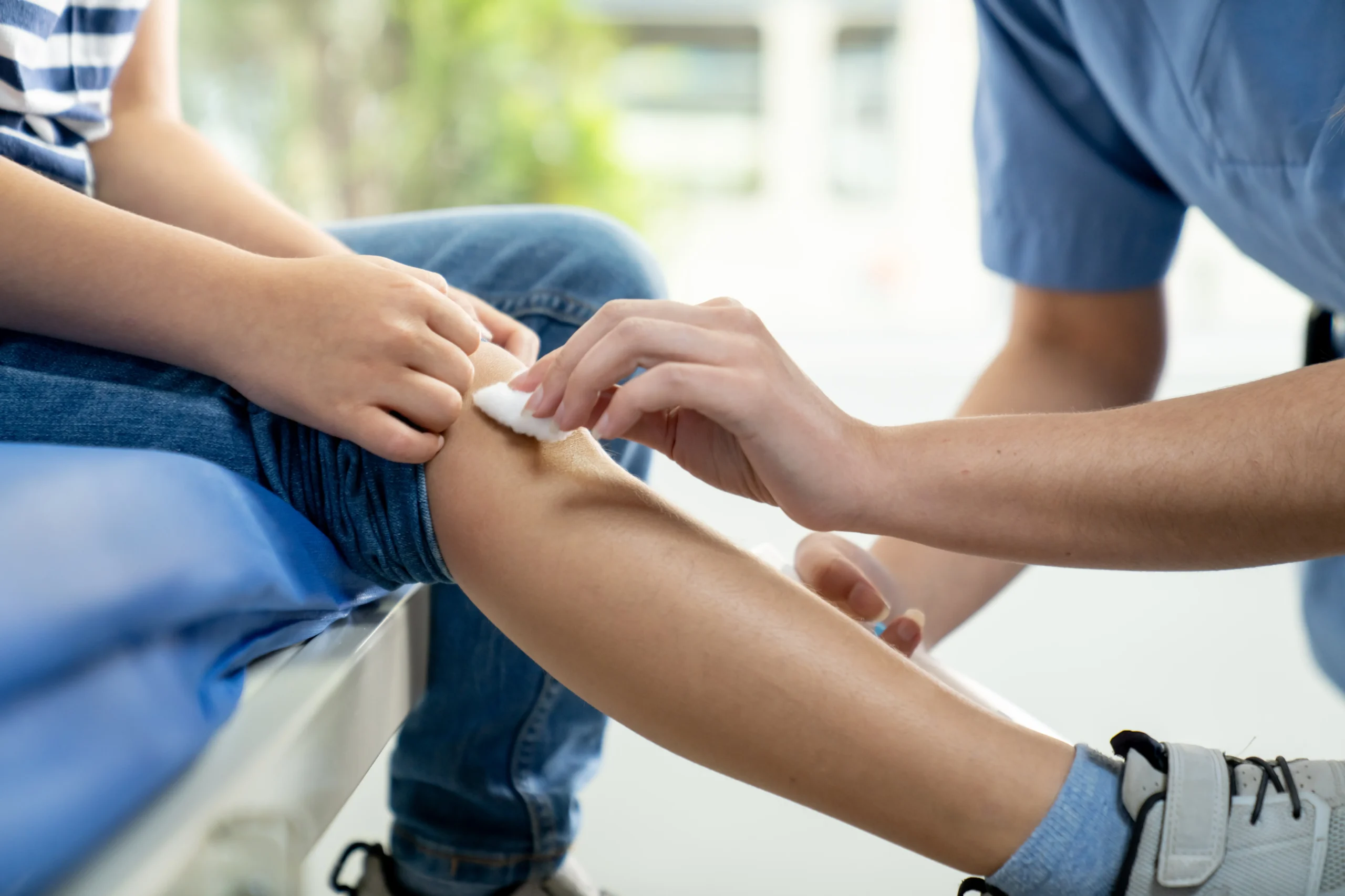 Adult cleaning a minor knee injury on a child’s leg with cotton wool