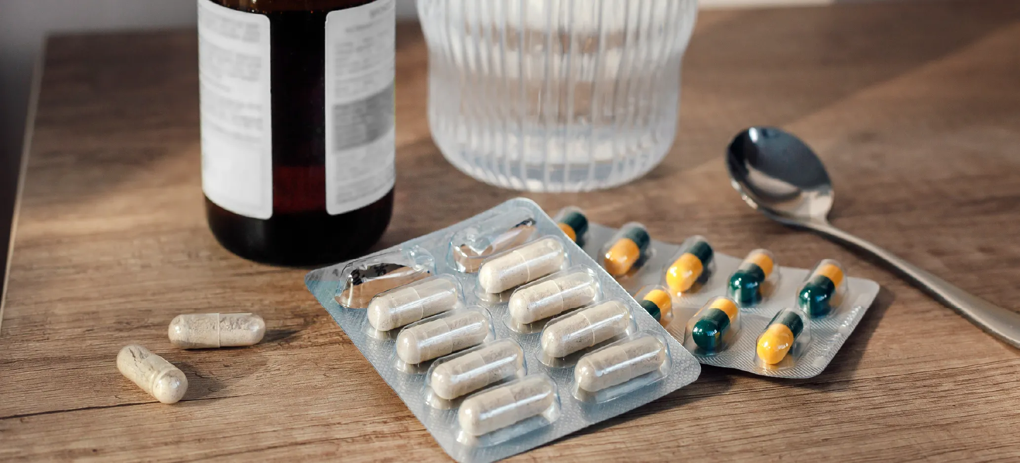 Medicine bottle, capsules and spoon on a table.