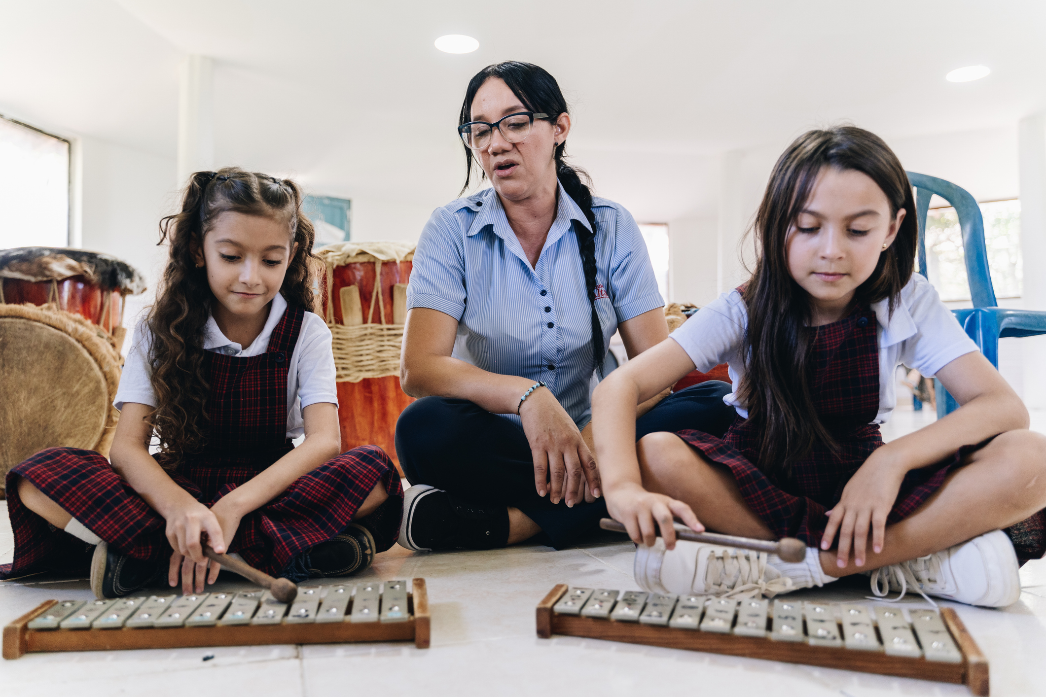Teacher helping two pupils play glockenspiels.