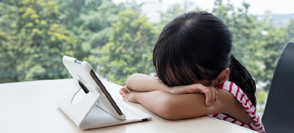 Child resting her head beside a tablet, appearing upset during online use