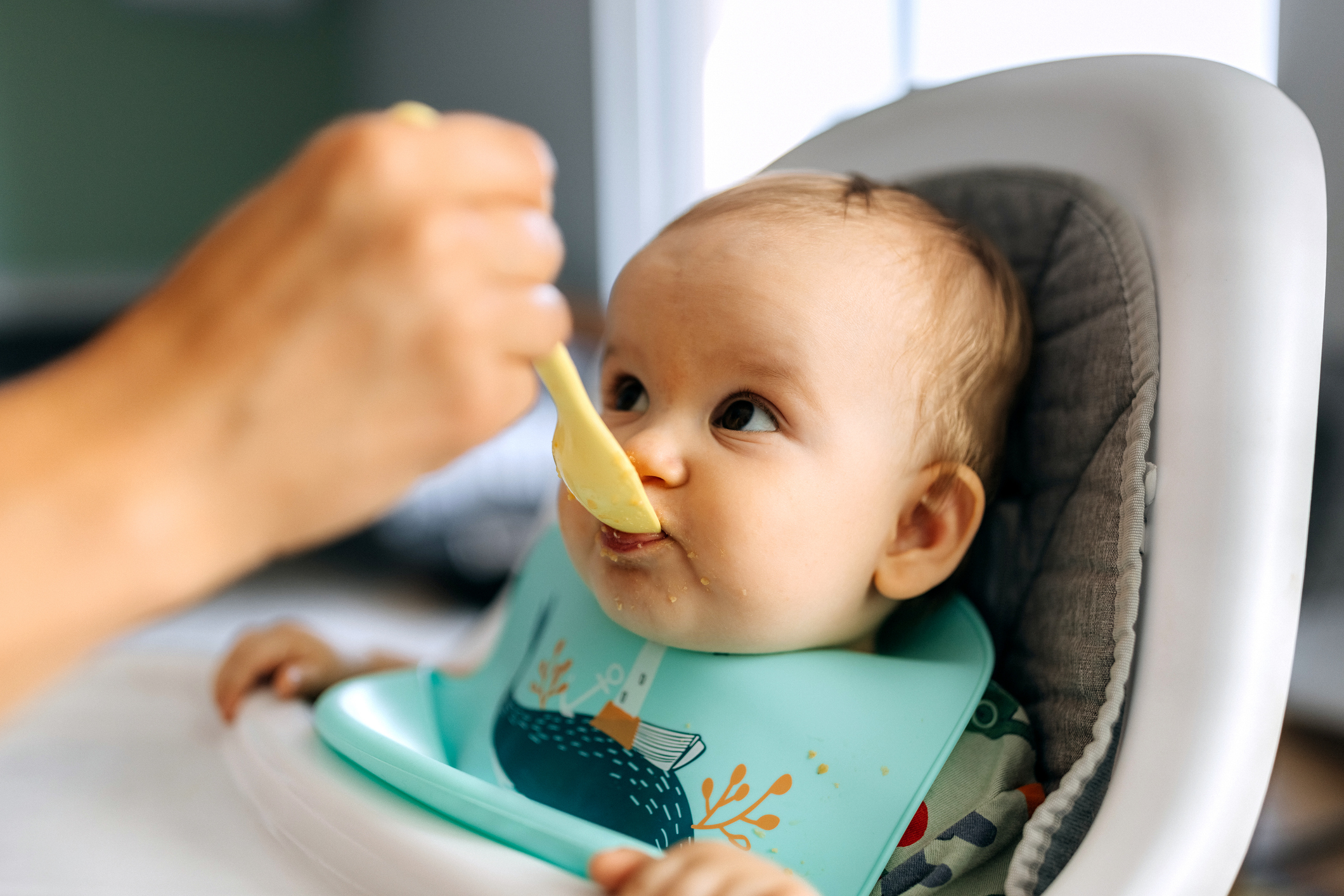Mother spoon feeding her baby boy at home