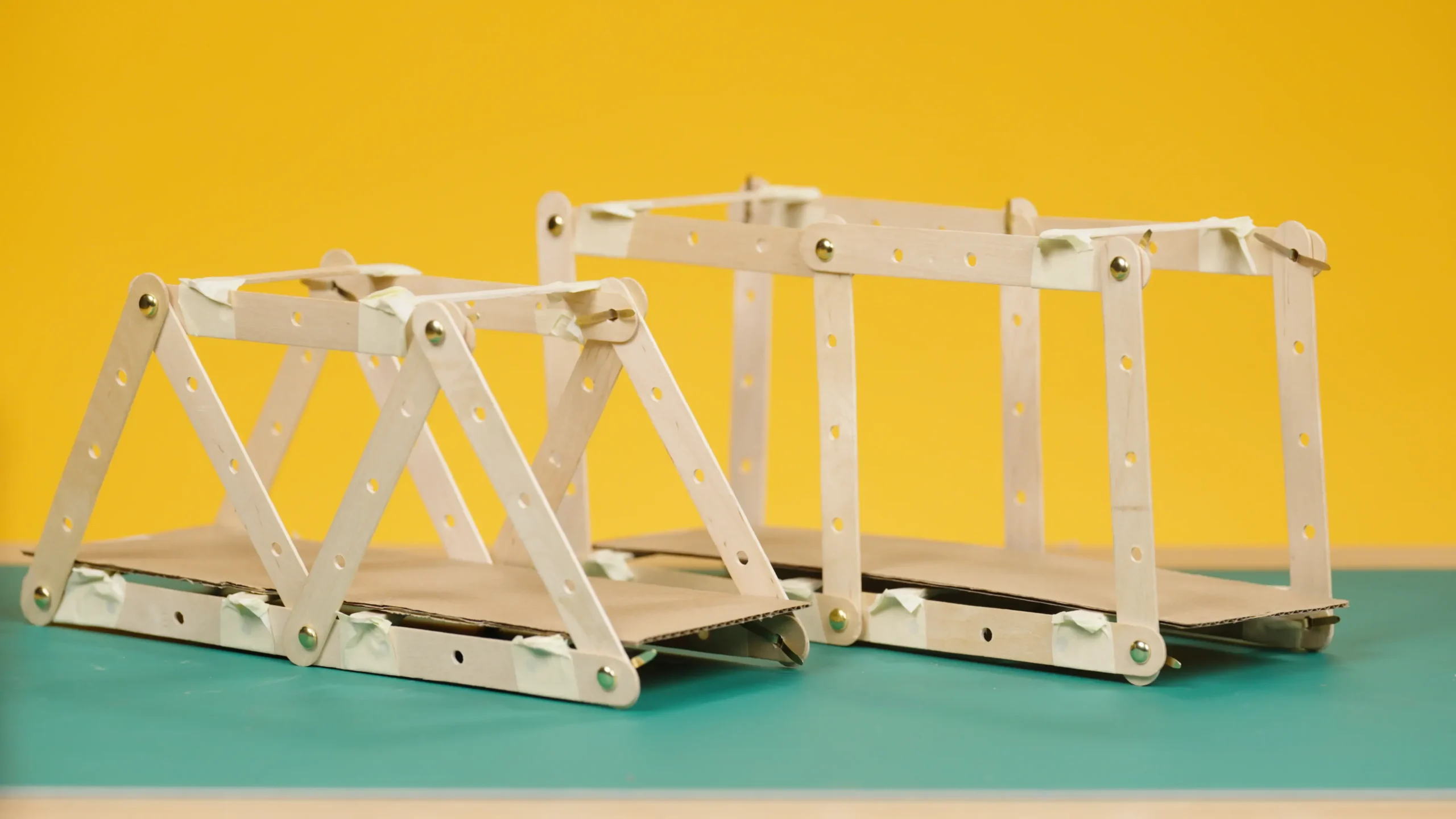 Models of truss bridges made from lollipop sticks and split pins. One is made from connected triangles and the other from connected squares.