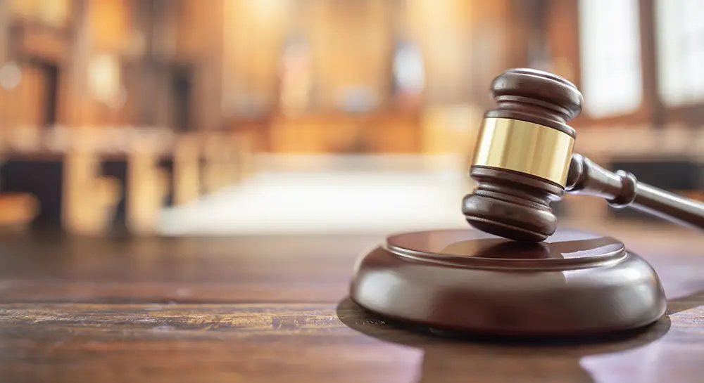 A wooden gavel with a gold-coloured band rests at an angle on a round wooden sound block.