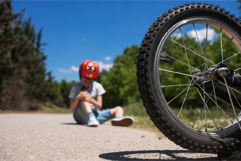 A child wearing a bicycle helmet sitting on the ground beside a bicycle wheel, holding their knee.