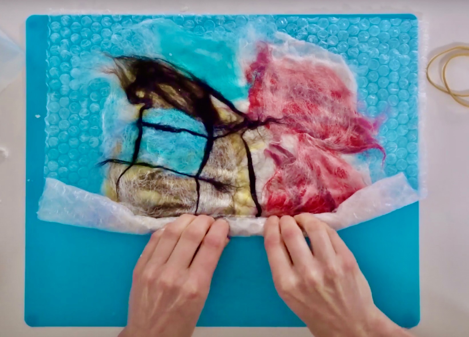 An adults hands rolling colourful wool fibres in bubble wrap to create a felt artwork.
