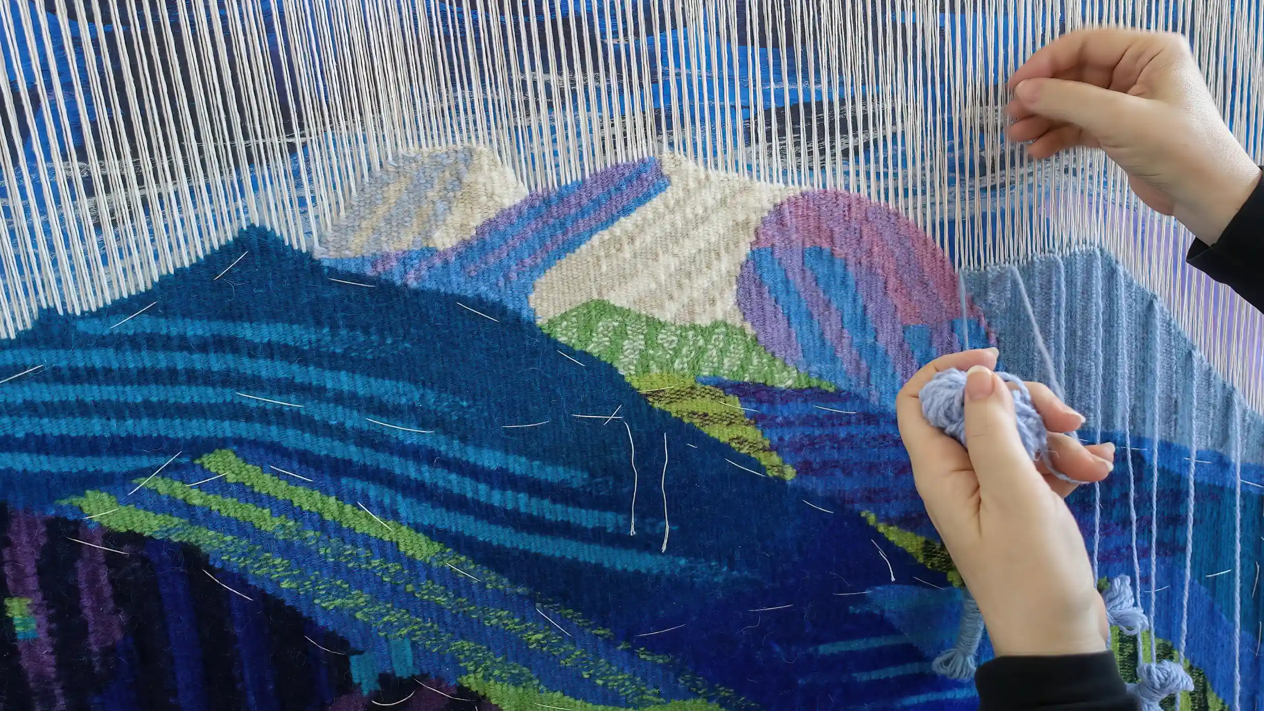 Hands weaving a colourful textile on a loom.