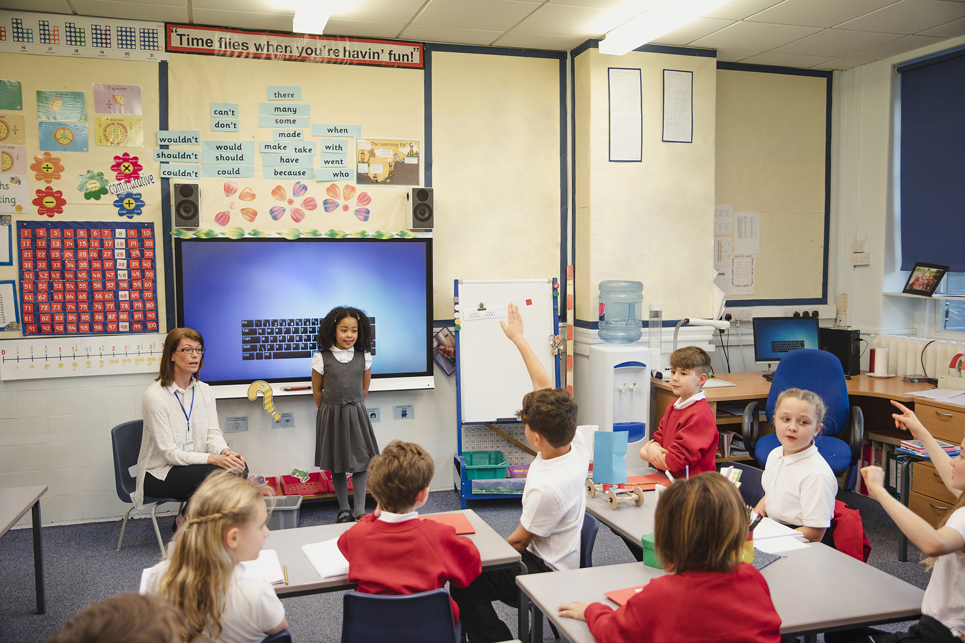 A primary schoolgirl presents her work to the class with the support of her teacher beside her. This is a school in Hexham, Northumberland in north eastern England.