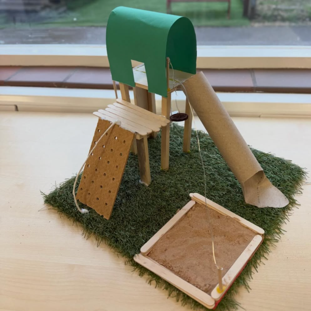 Model playground structure with slide and climbing wall made from craft materials.