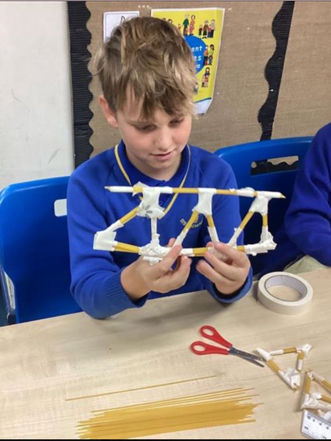Pupil examining a model bridge made from spaghetti and tape in class.