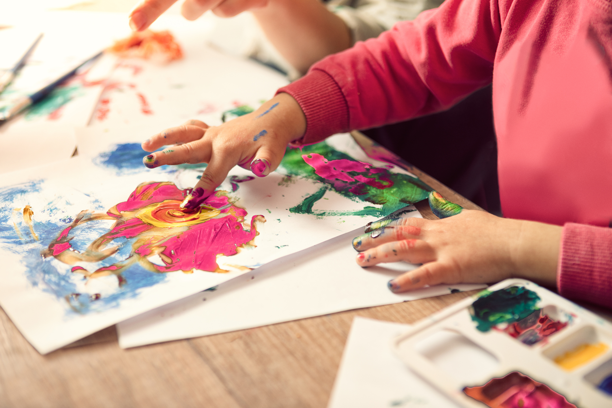 Child using finger painting to create colourful artwork.