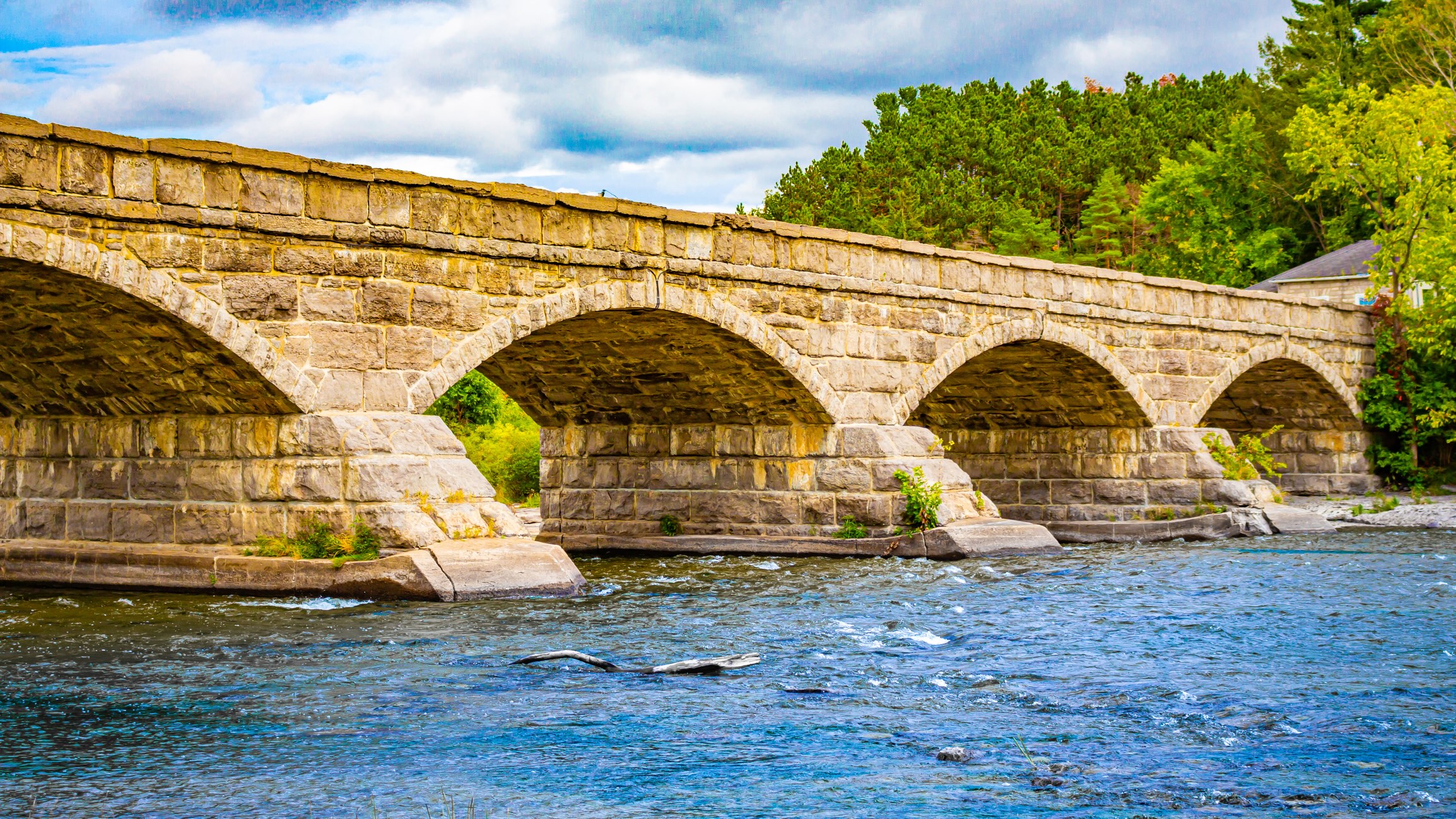 Old stone bridge with multiple arches spanning a shallow river.