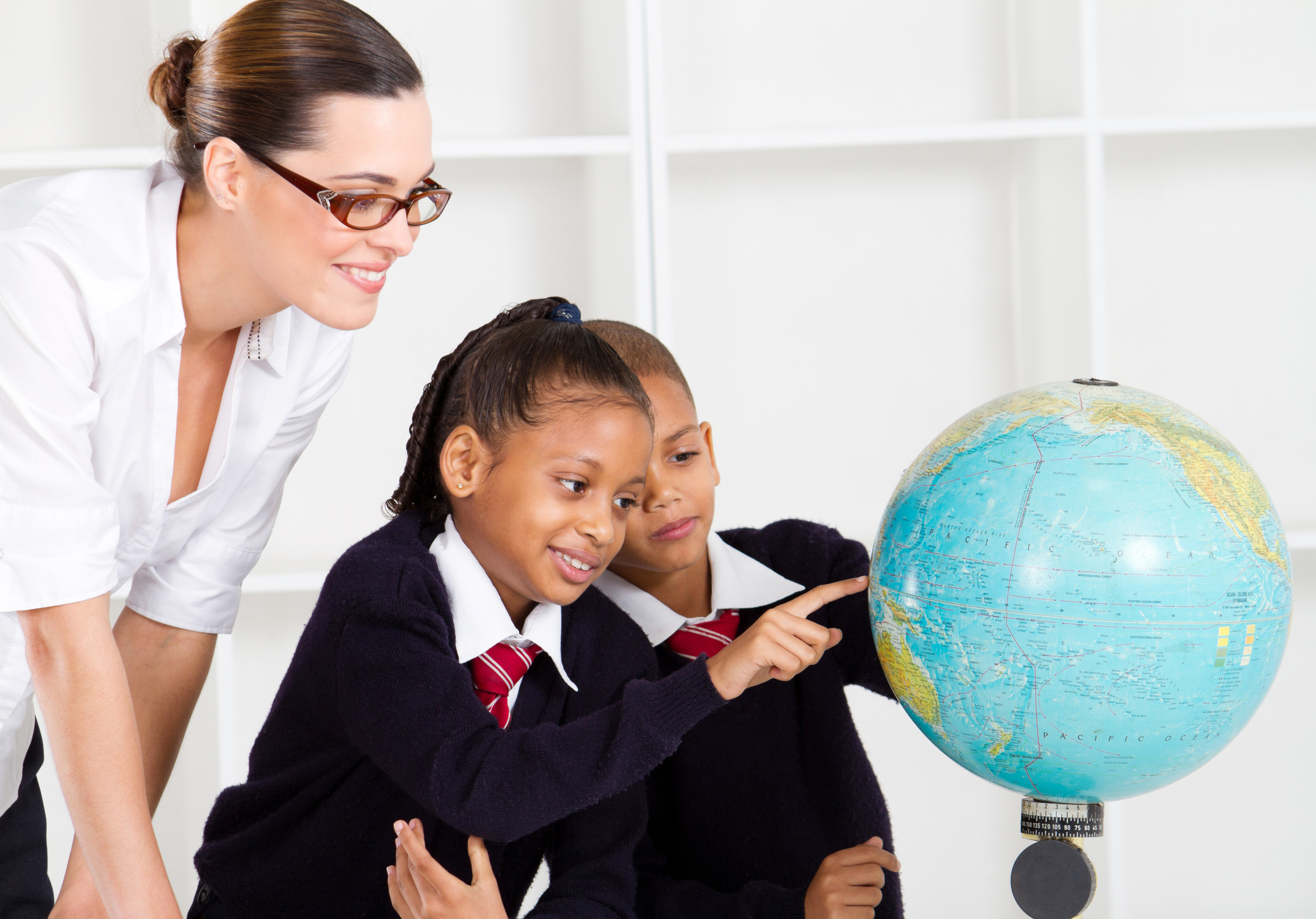 Teacher with school children pointing out countries on a globe.