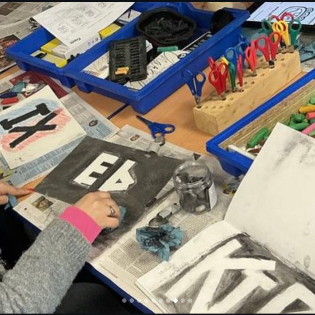 Pupil blending charcoal around bold letter shapes during an art lesson.