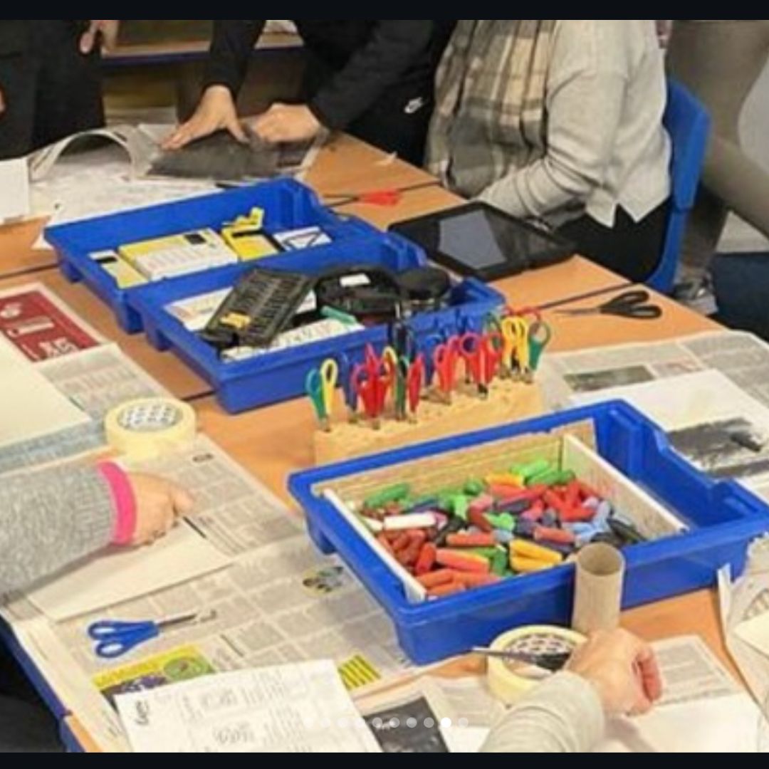 Classroom art table with trays of oil pastels, scissors and newspapers.