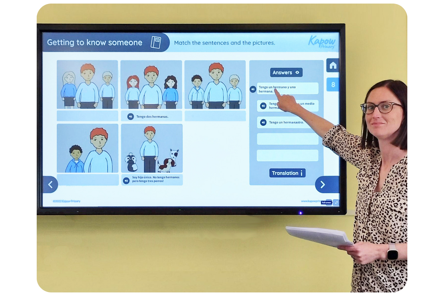 Teacher stood in front of an interactive whiteboard pointing to a presentation in Spanish