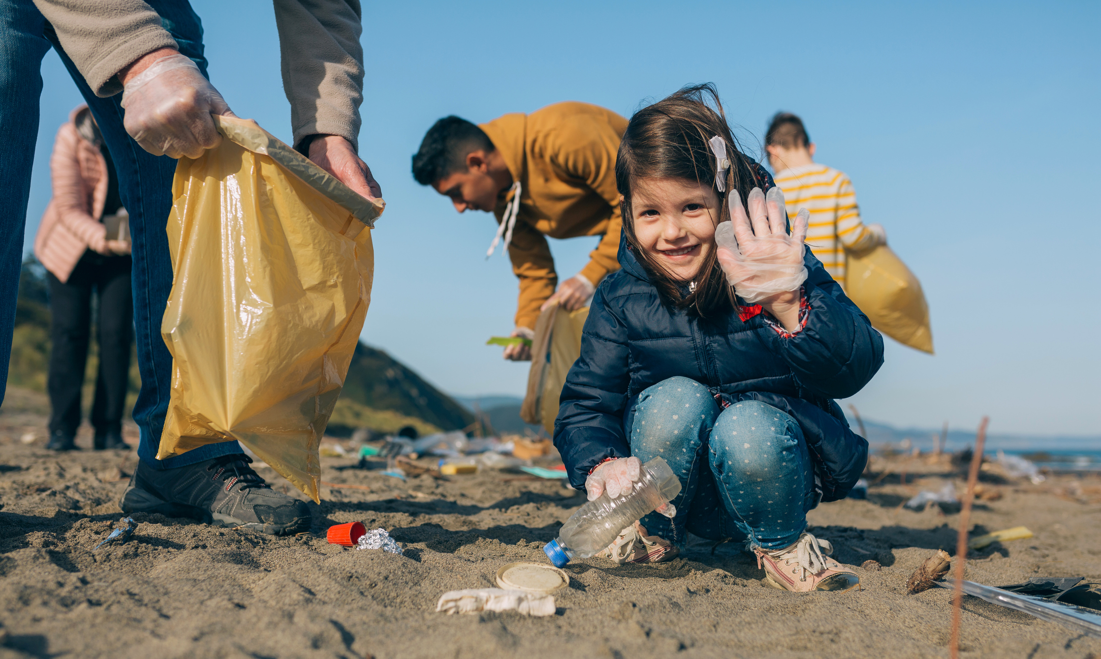 A happy girl picking up trash with volunteers on a beach, helping clean the environment.