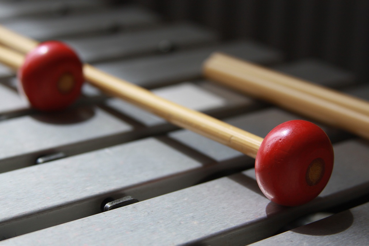 Two mallets with red heads lie across the metal bars of a percussion instrument.