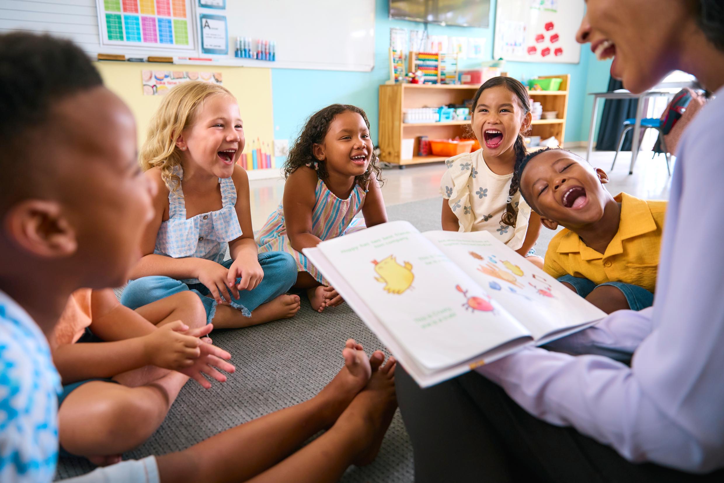 Group of young children laughing during a storytime session in a classroom.