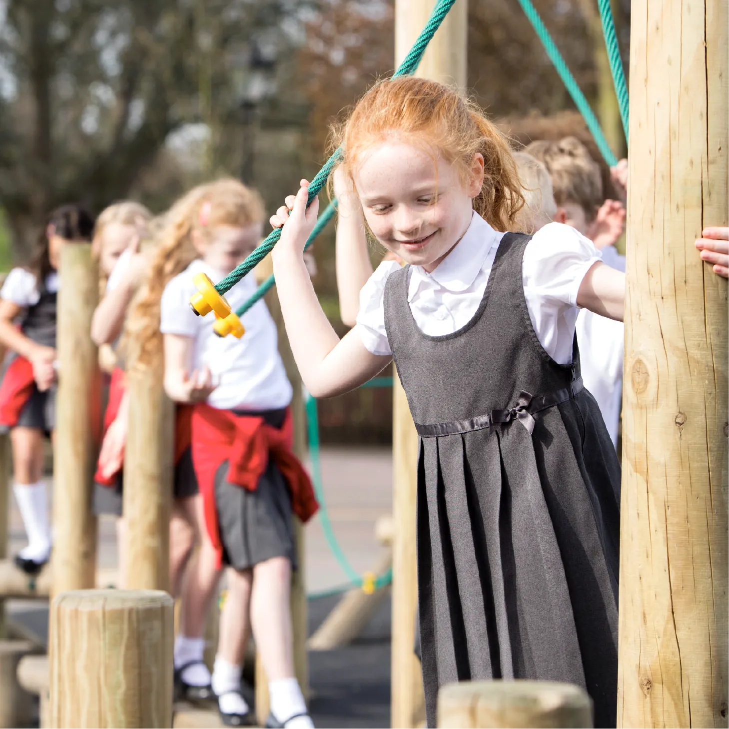 A line of pupils along an outdoor obstacle course, balancing on logs and holding onto ropes.