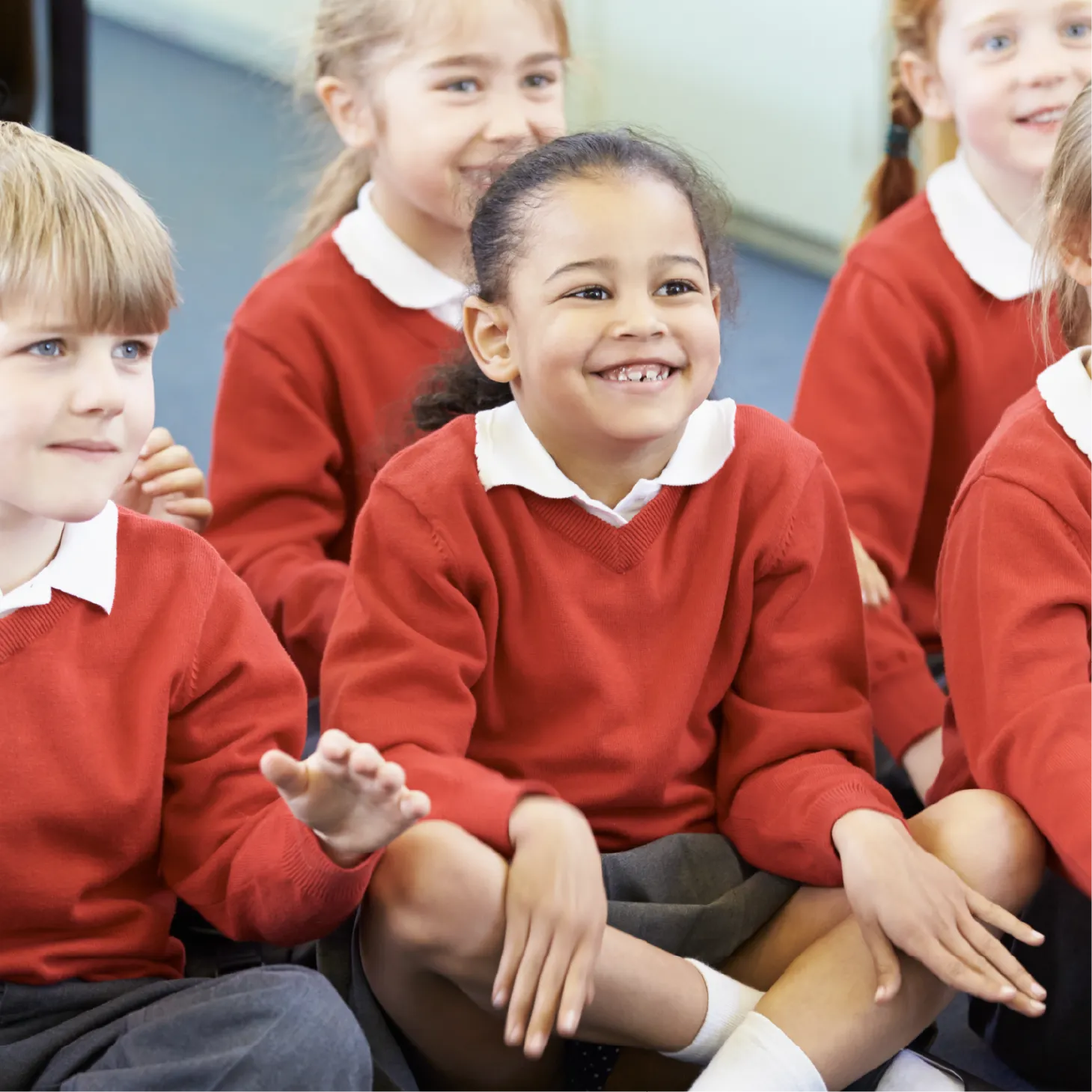 A group of primary school children sitting on the floor, cross-legged, smiling.