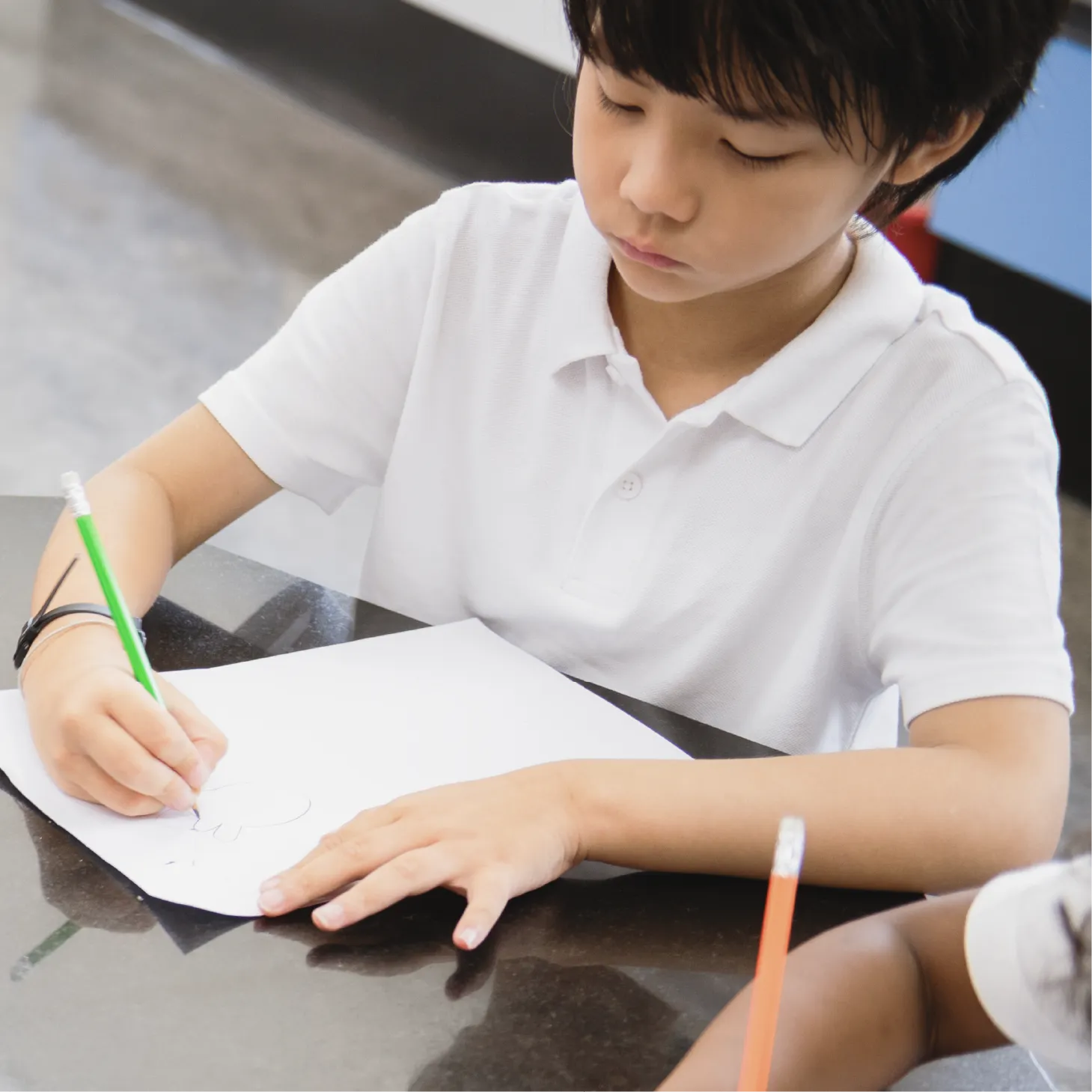 A young boy is concentrating while drawing with a pencil.