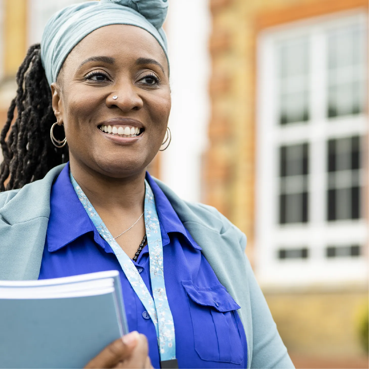 A smiling member of school staff, holding some exercise books, outside the building.