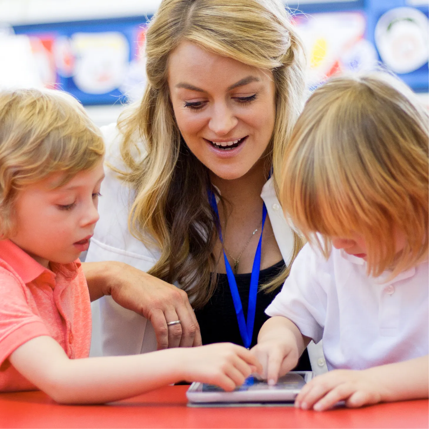 A teacher guiding two pupils as they use an electronic tablet.