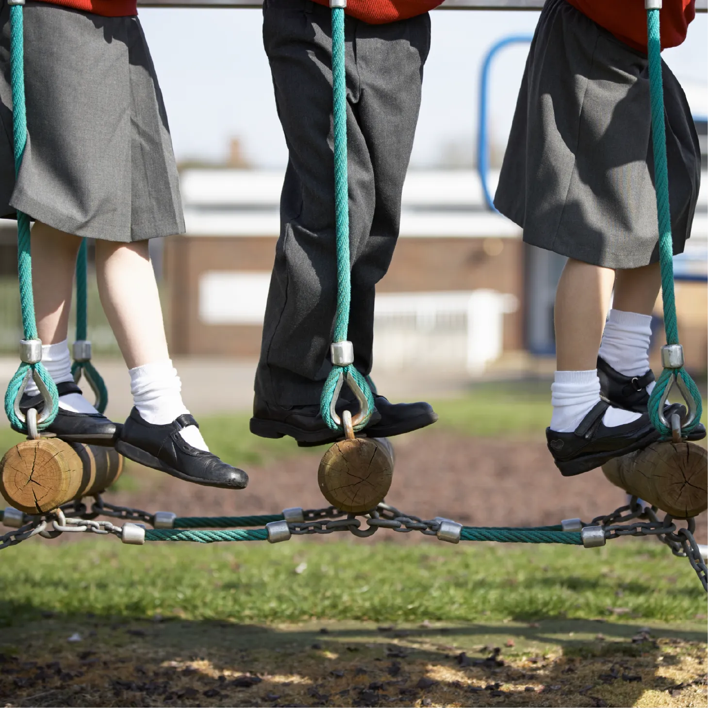 Children tackling a wooden log obstacle course outdoors, stepping from log to log to cross a bridge.