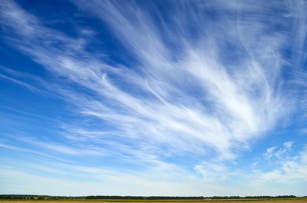 Feathery cirrus clouds spread across a clear blue sky over the countryside.