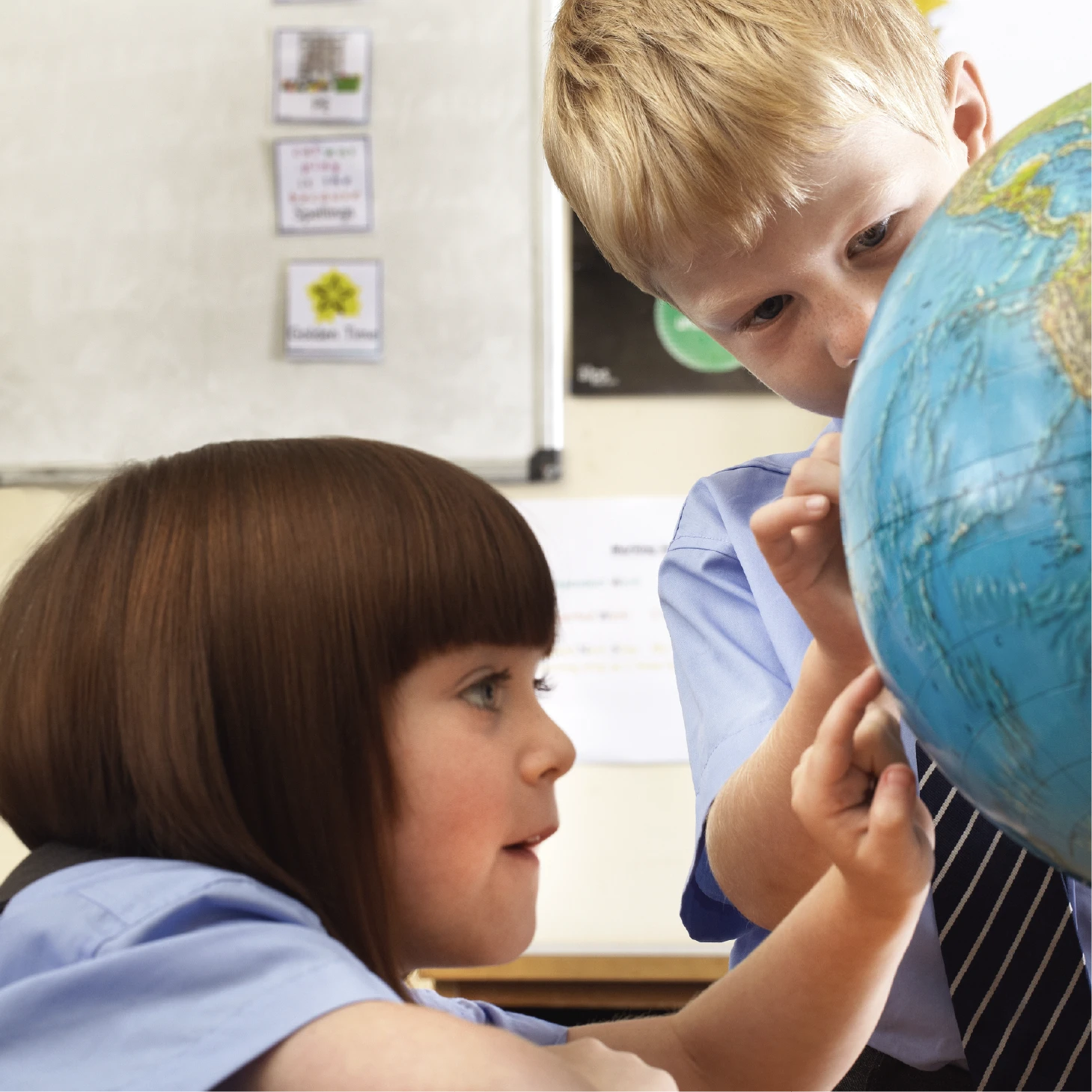 Two pupils using a globe in the classroom, pointing to locations and exploring world geography together.