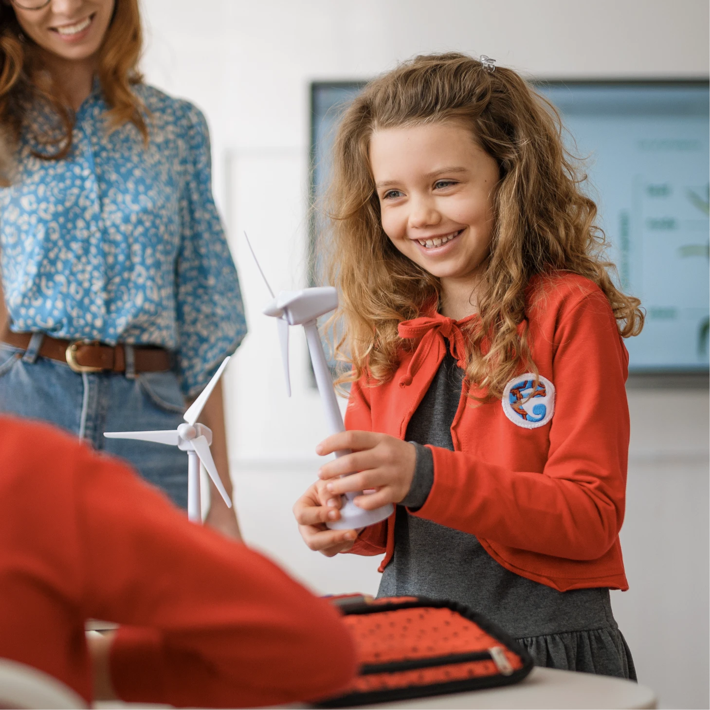 A young girl holding a model wind turbine shows another pupil in class.