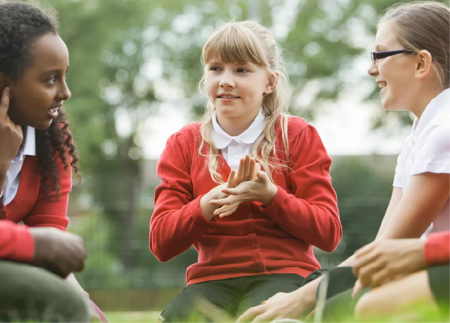 Three primary school girls sitting outdoors on the grass talking.