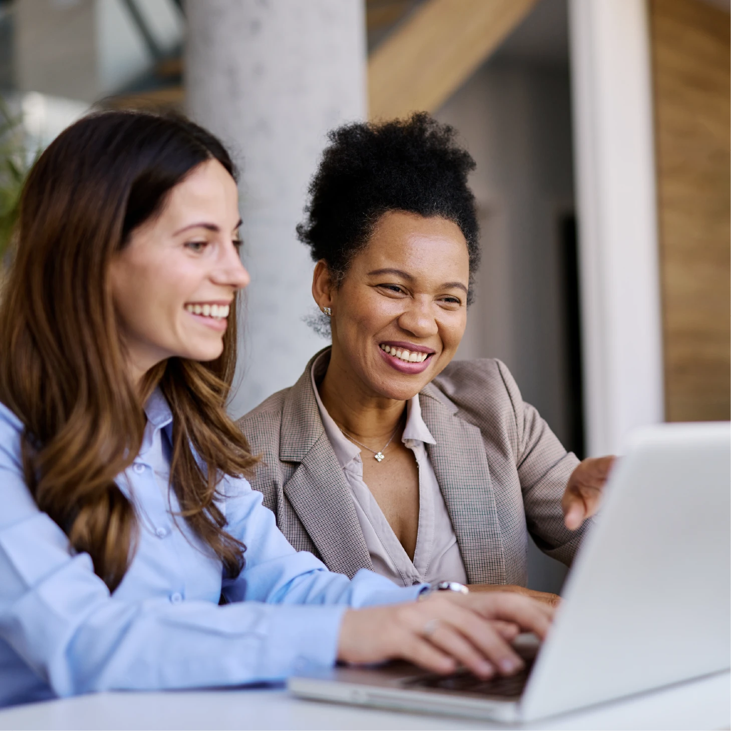 Two colleagues smiling and working together on a laptop during a meeting.