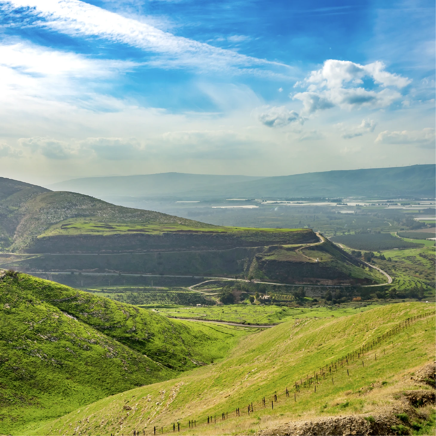 Rolling green hills and a broad valley landscape beneath a blue sky with scattered clouds.