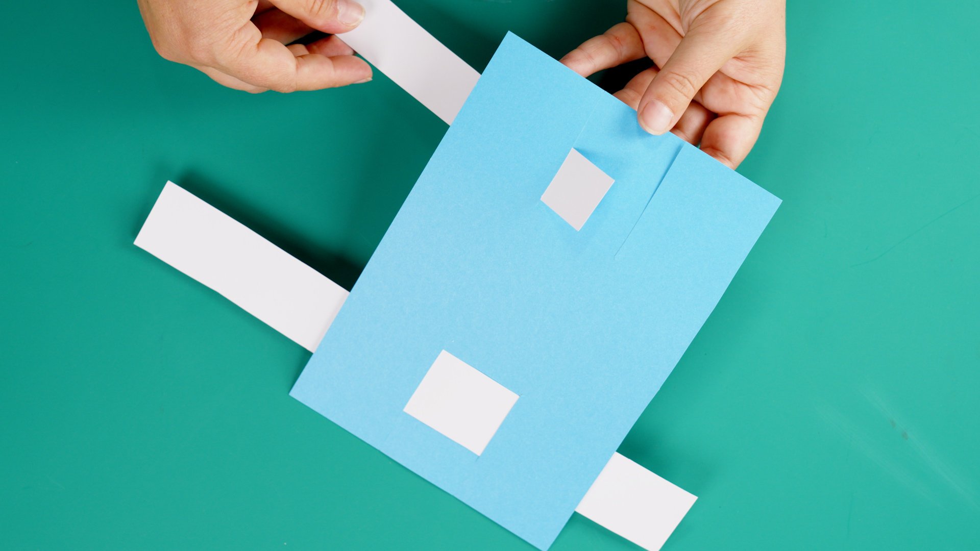 Image of hands weaving a card slider through slots to make a matching game in D&T.