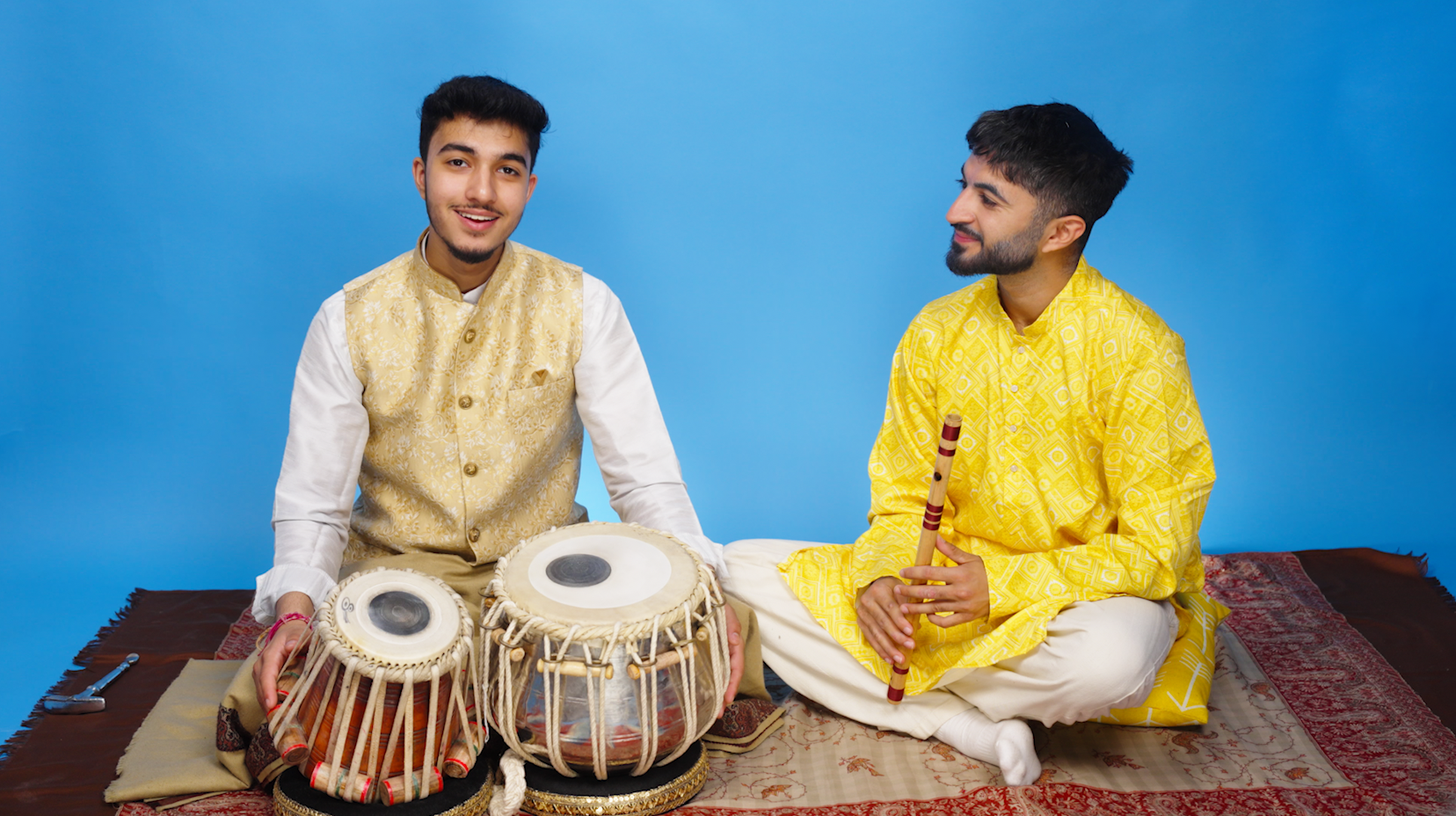 Two musicians sit together with traditional instruments ready for a performance