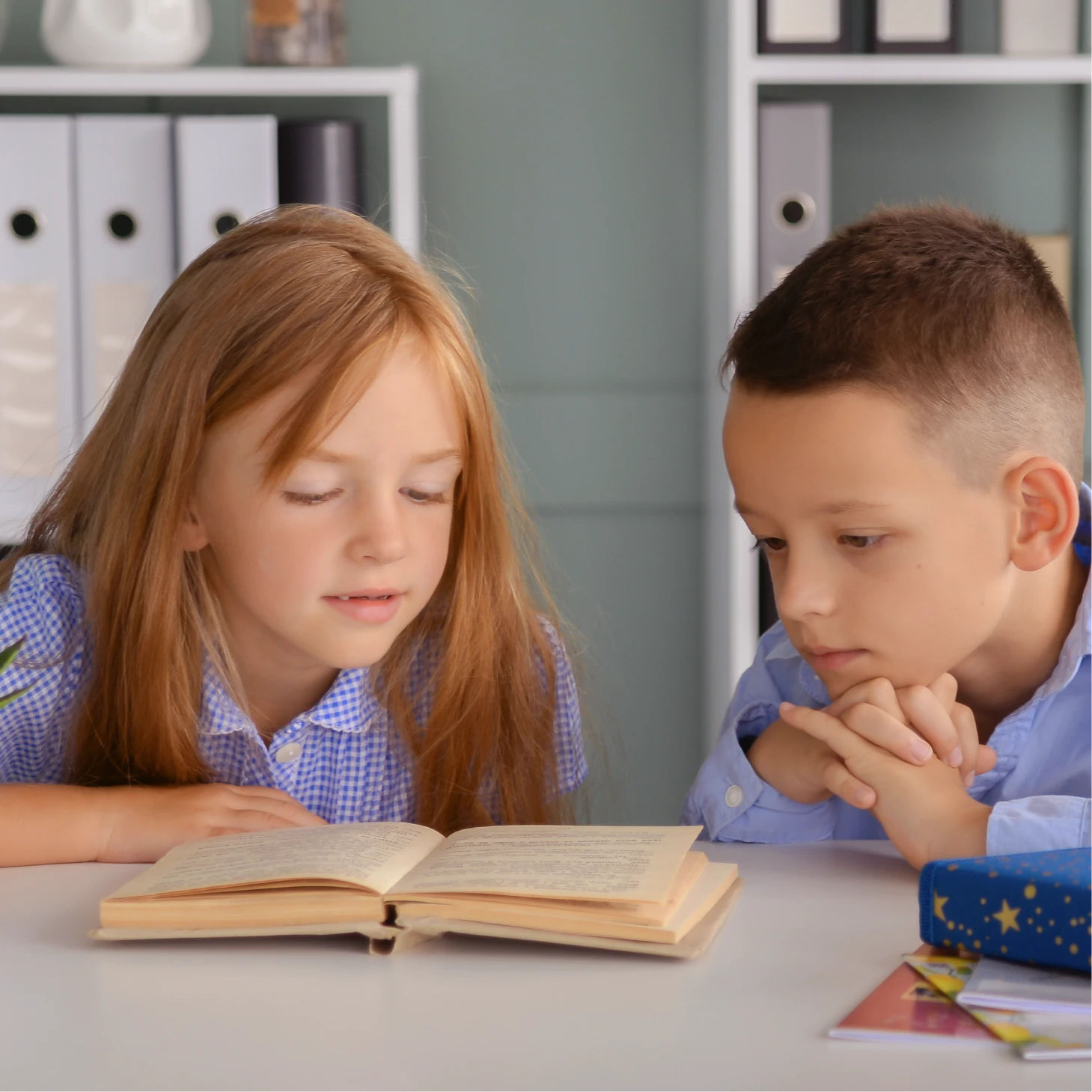 Two young children reading a book together at a table.