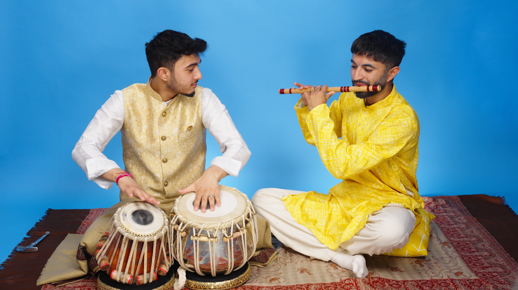 Two musicians perform together using traditional instruments against a simple backdrop