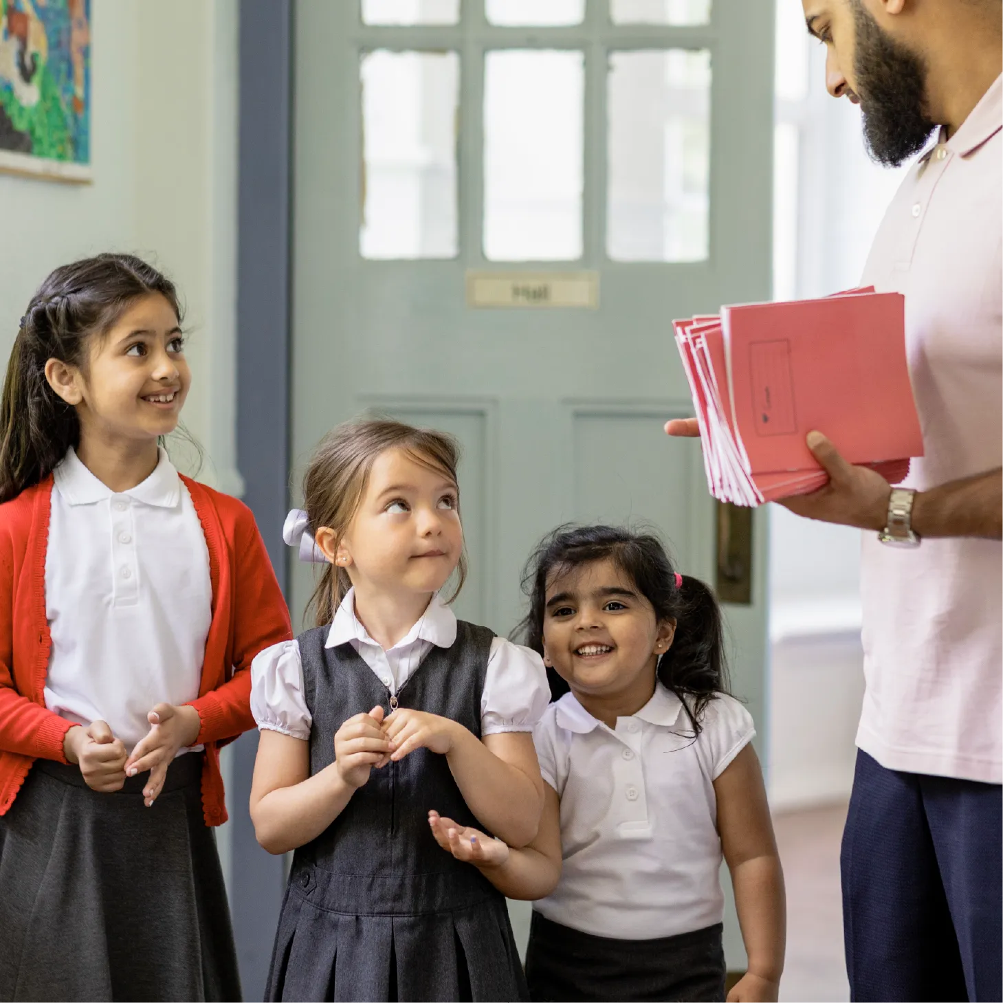 A teacher is speaking with children in the corridor while holding some exercise books.