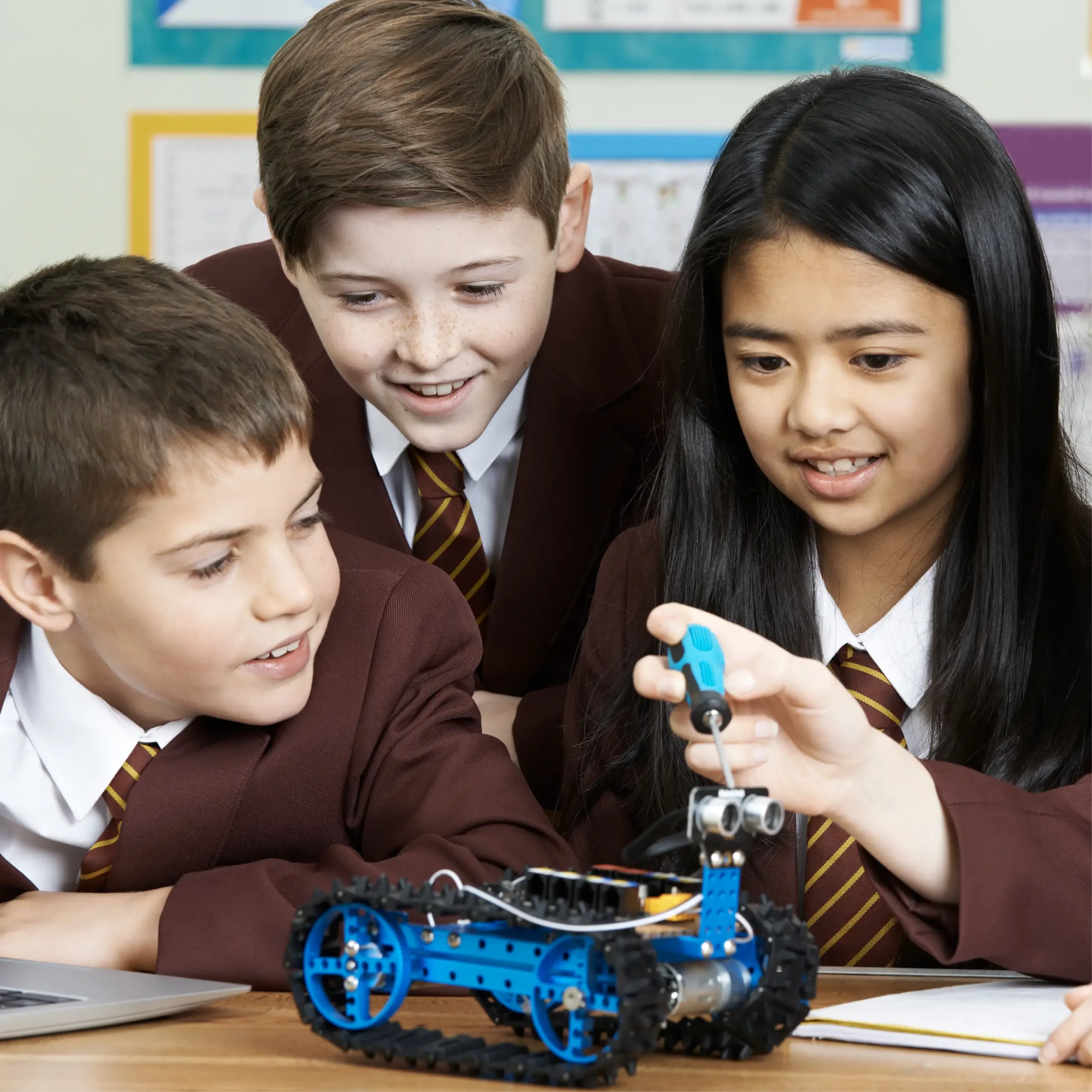 Three happy pupils wearing blazers and ties look at a small model vehicle.