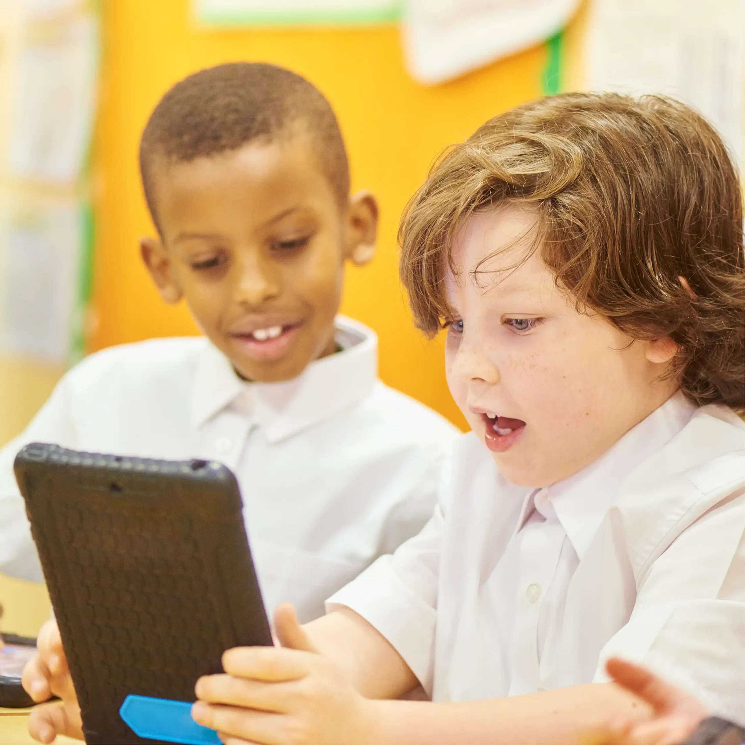 Two excited boys wearing school uniform look at a tablet.