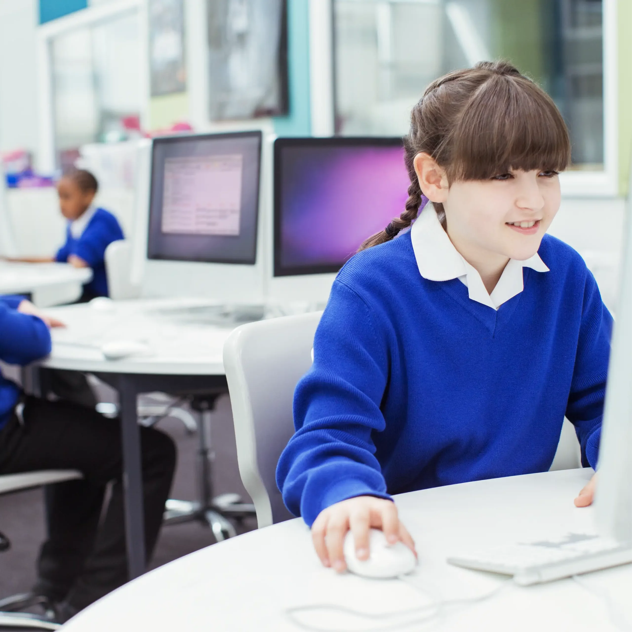 A girl wearing blue uniform sits in a classroom and looks at a computer.