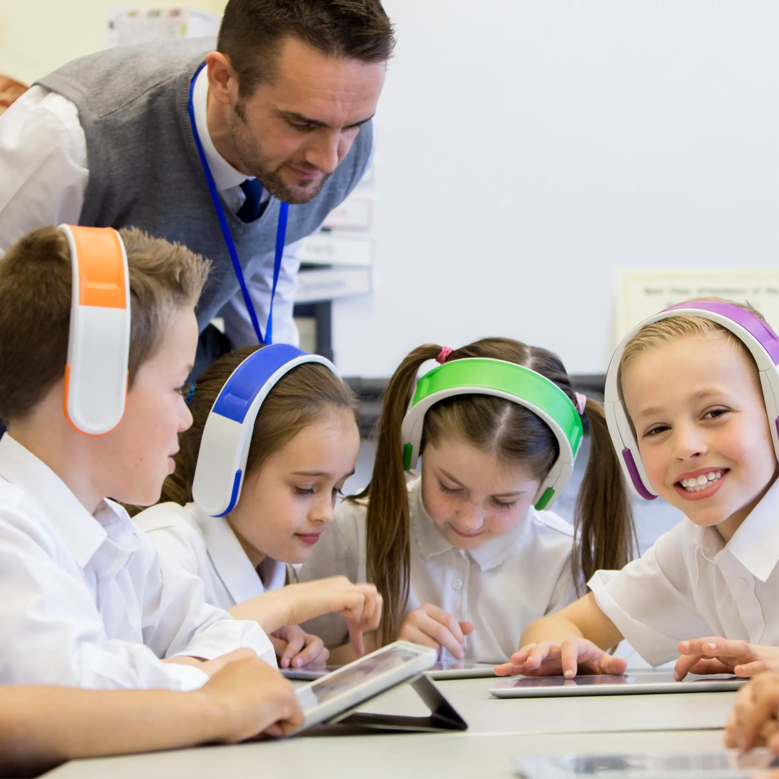 Four pupils wear colourful headphones and look at tablets as a teacher watches what they're doing.
