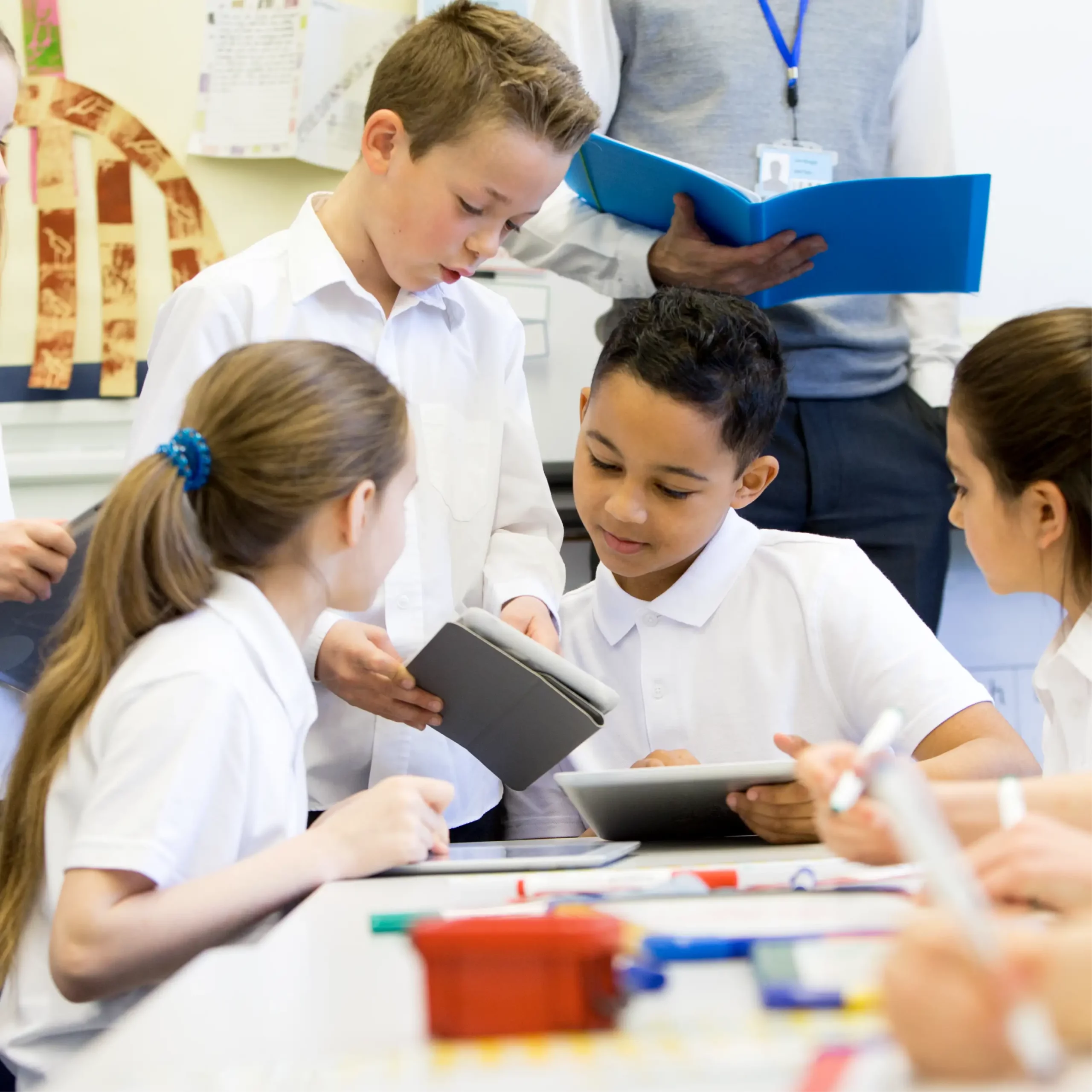 Primary school children working together using tablets at a classroom table.